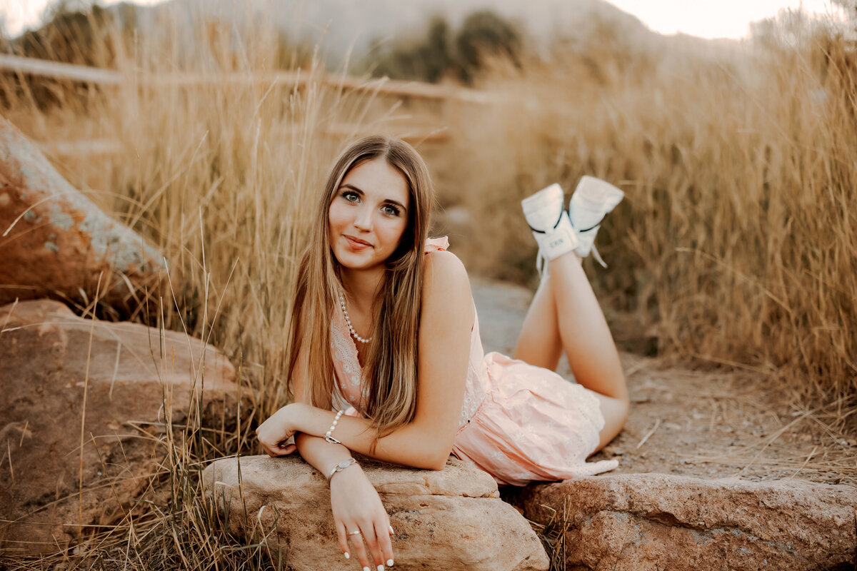 High school senior girl laying on her stomach with her legs crossed behind her on a large rock in Boulder, Colorado