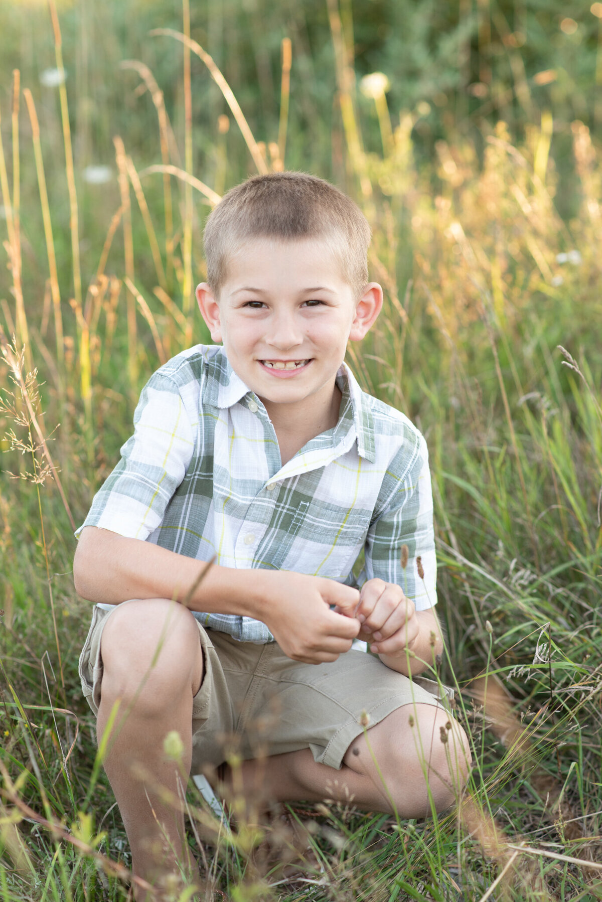 Young boy squatting in field at sunset