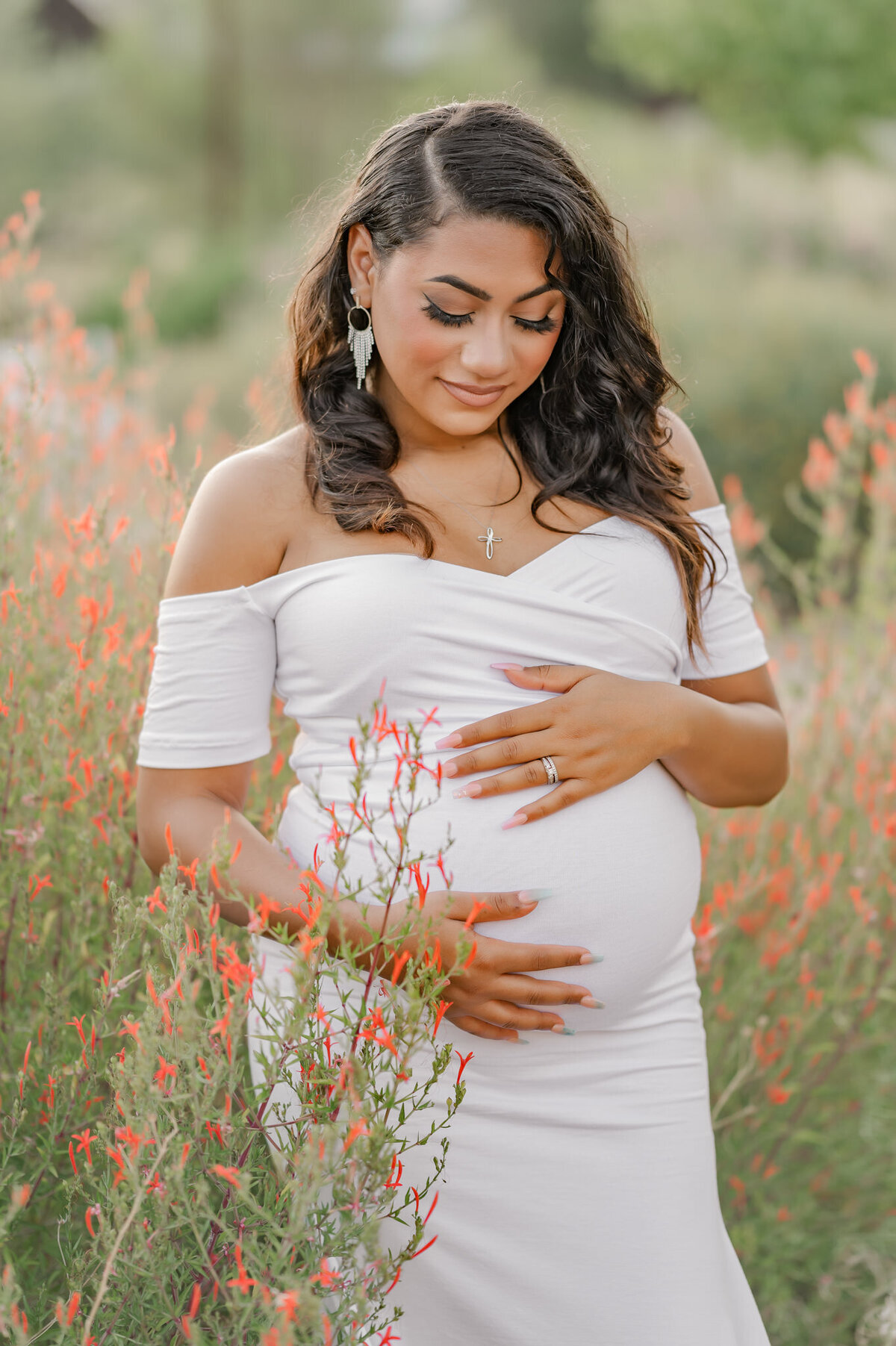 Maternity photography of an expecting woman gazing at her belly, surrounded by red flowers.