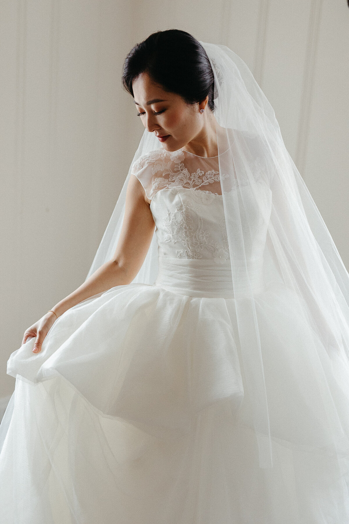 Light-filled portrait of a bride loving her elegant wedding dress.
