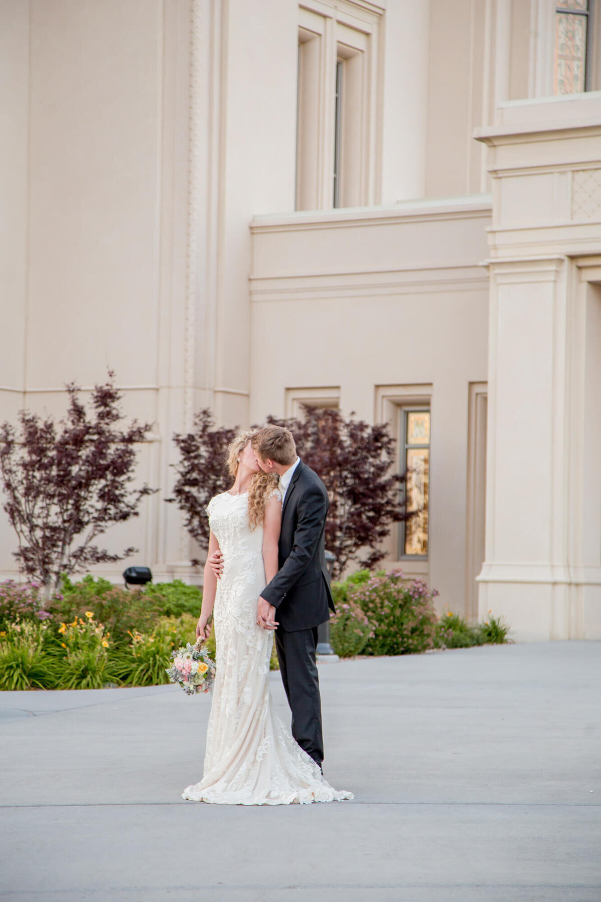 a wedding coulpe kissing in front of a stone buildingg