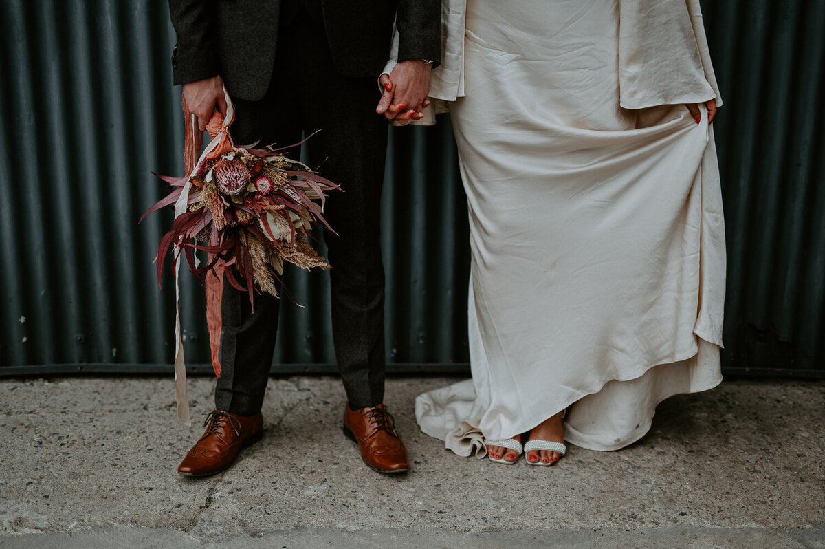 Details of a couple that married at White Syke Fields. The bride is wearing a boho wedding dress and the groom is wearing a tweed suit and carrying the brides dried bouquet.