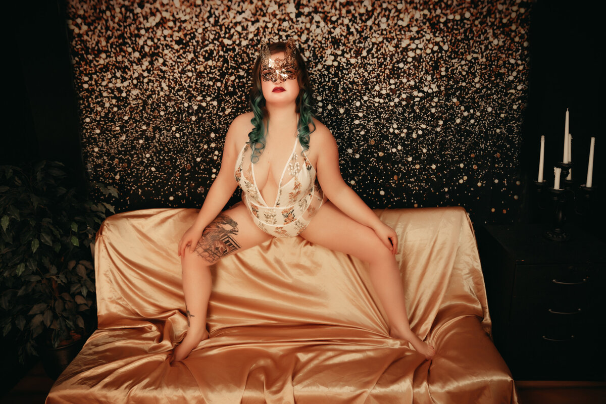 Woman sitting on top of gold couch with glitter background she is wearing a gold mask and floral lingerie in Minnesota