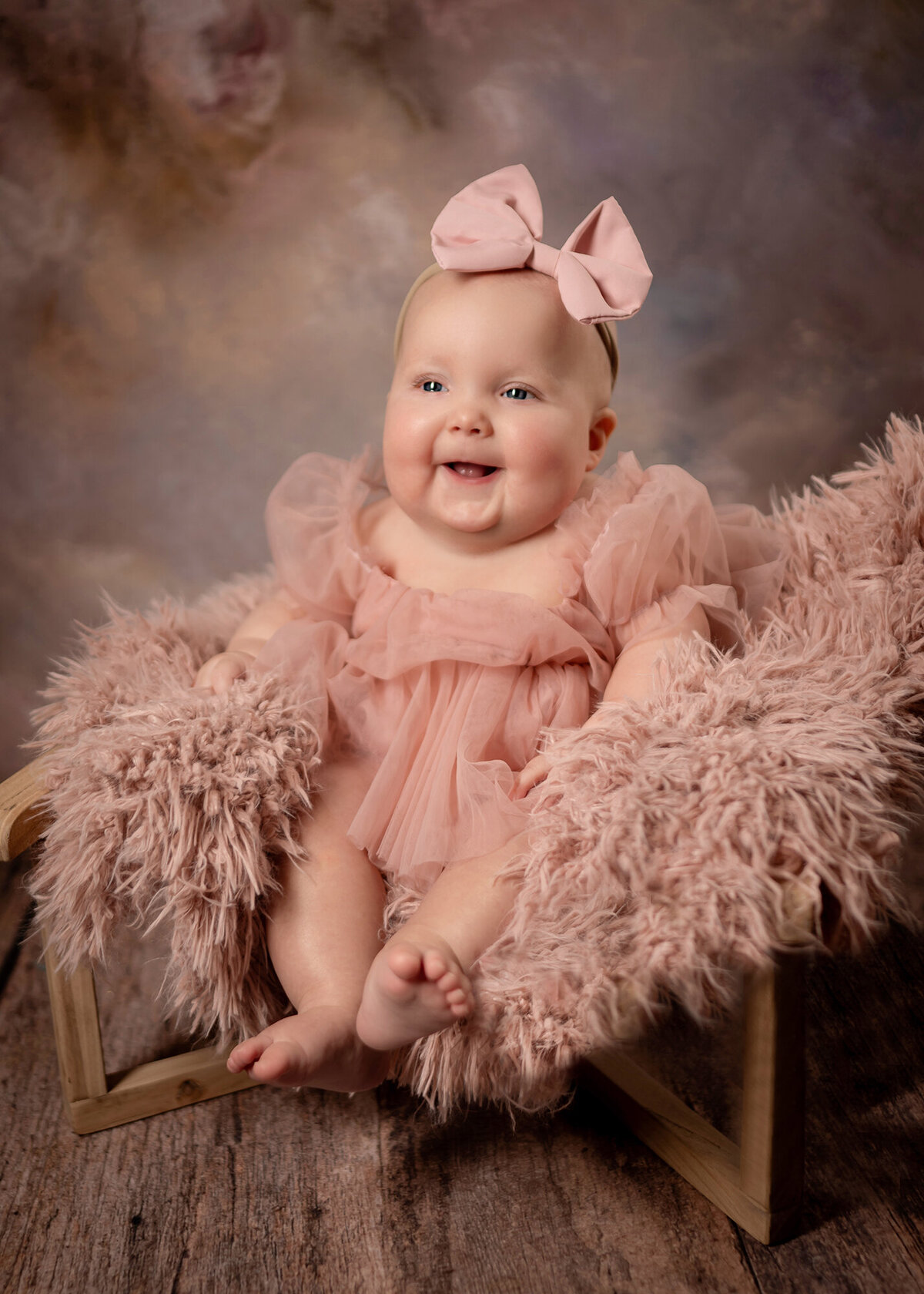 A baby girl laughs while she sits on a fluffy pink chair and wears a pink tutu