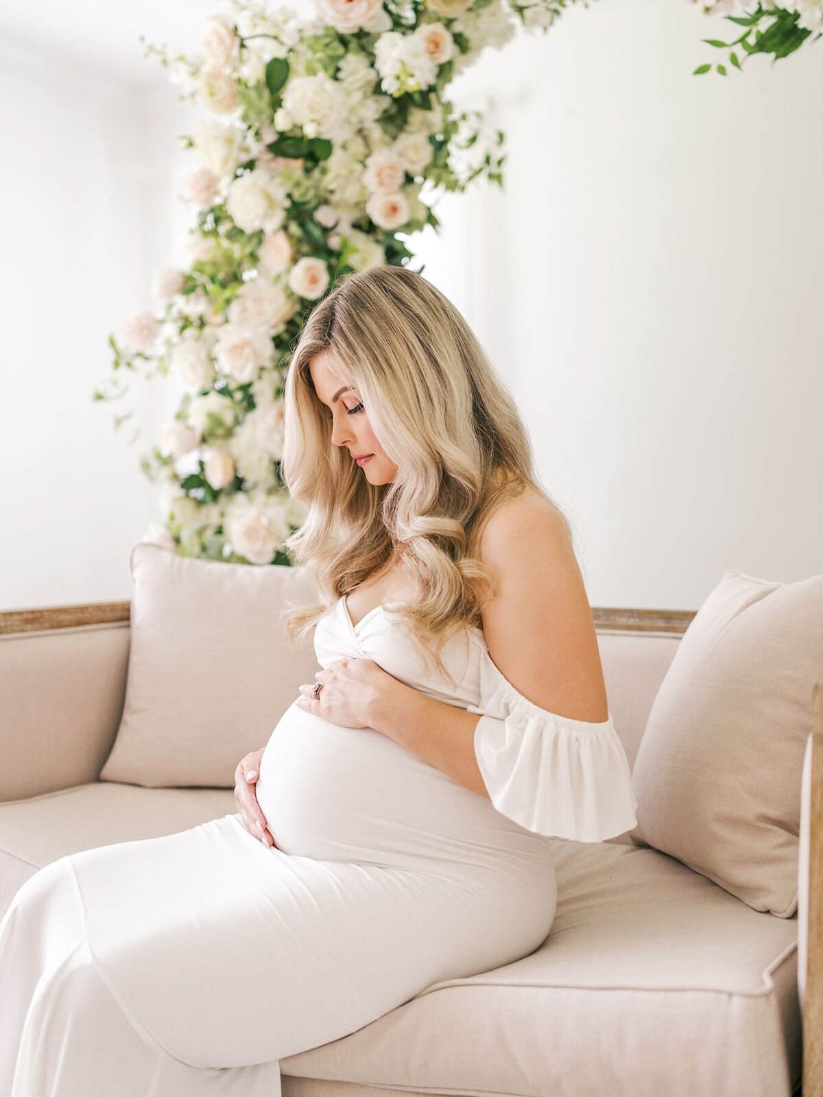 Expecting mother sitting in a studio decorated with flowers holding her belly.