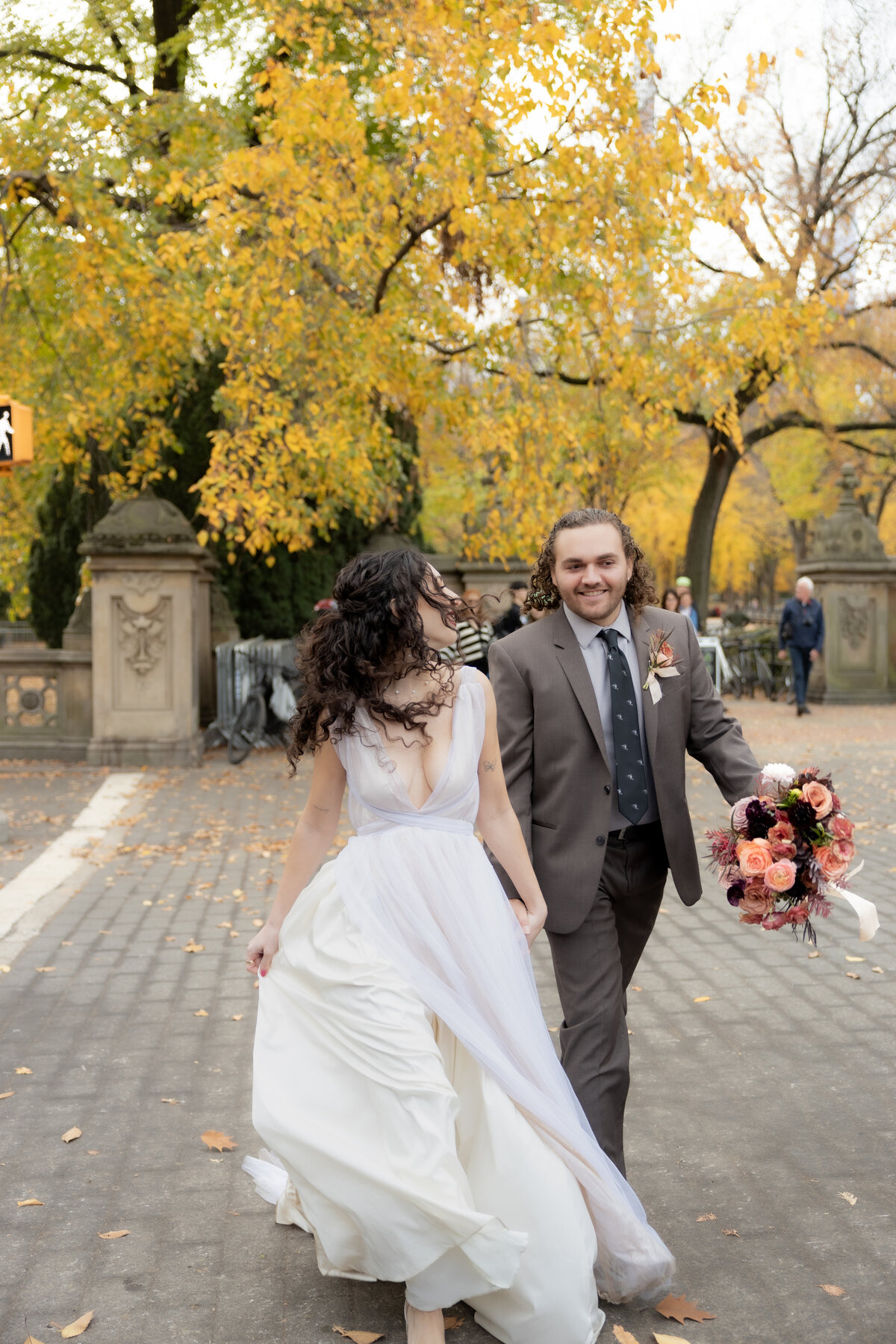 The bride laughing joyfully while holding her bouquet among autumn leaves in Central Park.