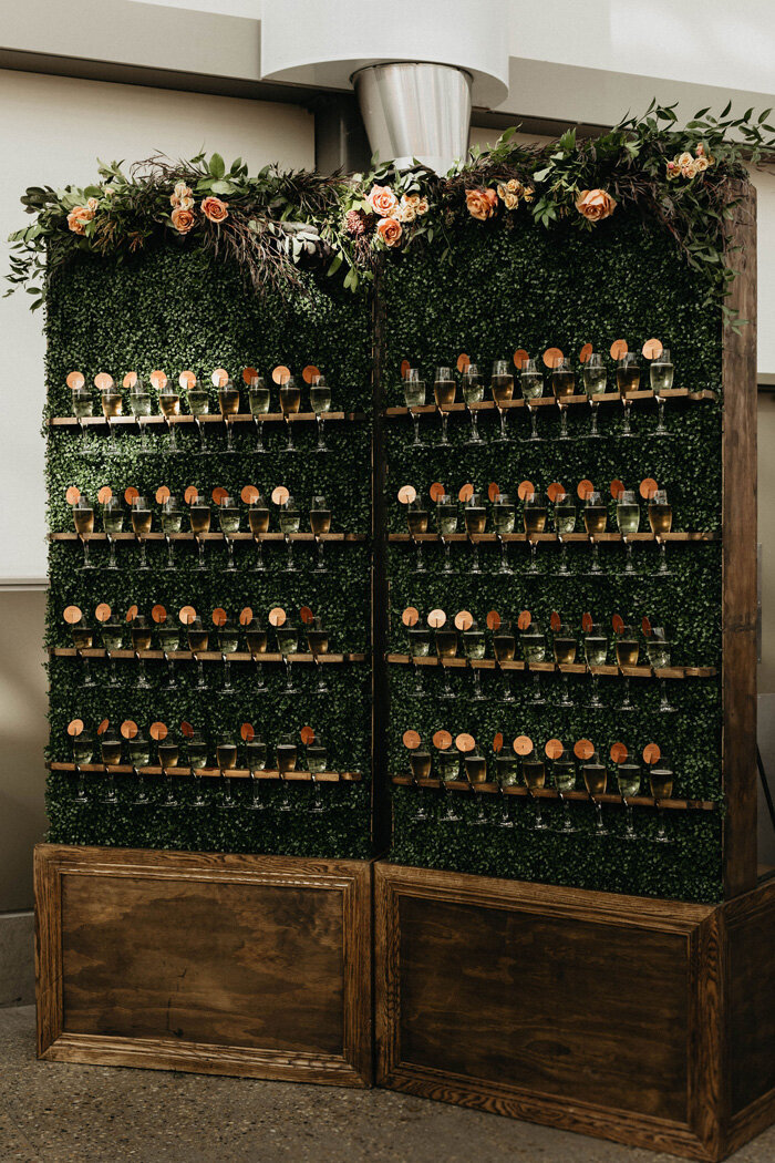 Champagne wall at the wedding reception with greenery.