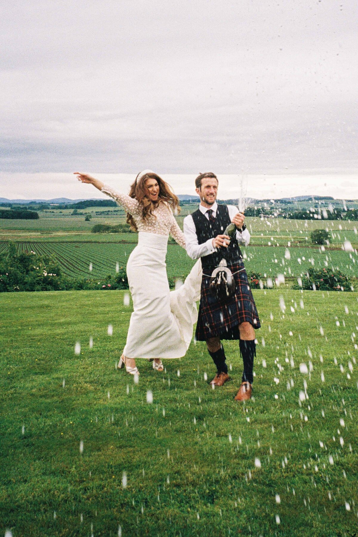 A bride and groom spray prosecco and jump with joy.