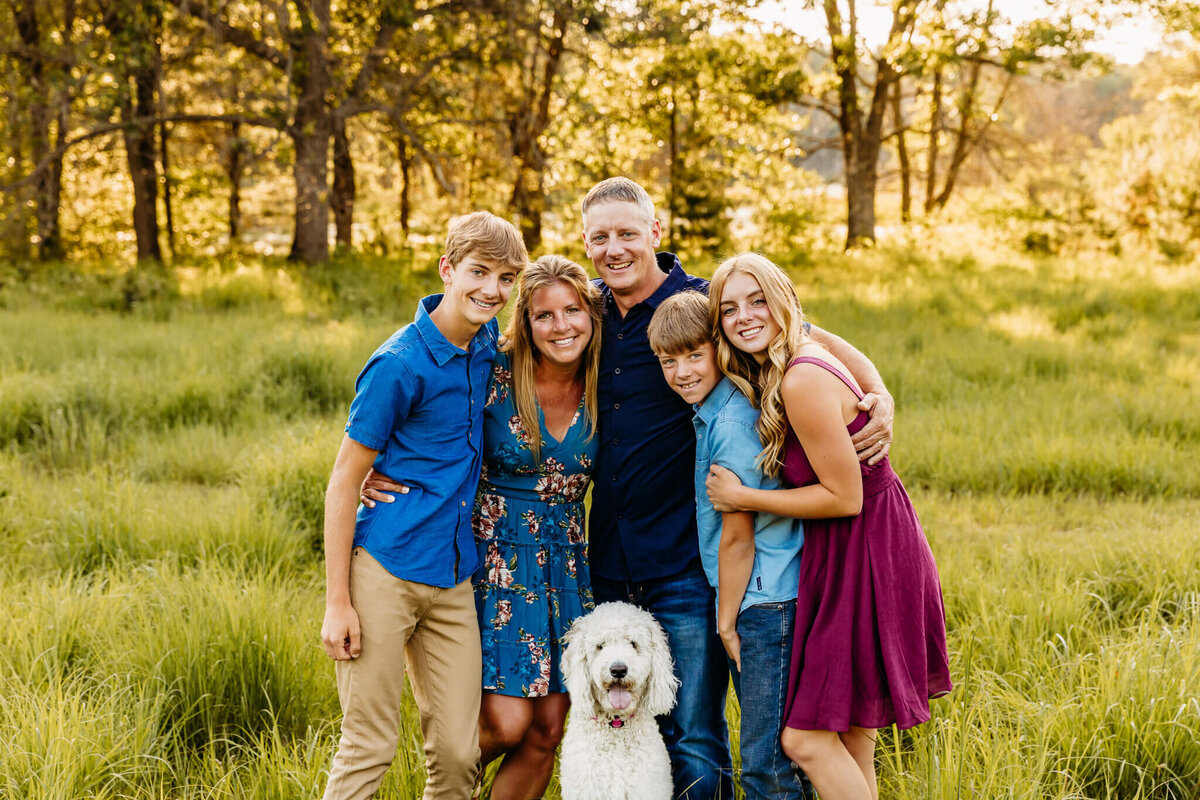 beautiful family of five hugging each other with their white poodle in front during family photography session