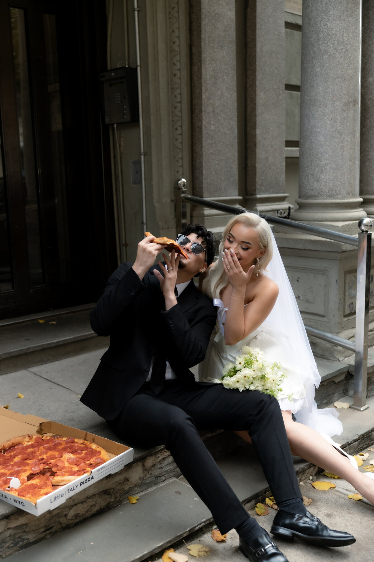 Bride and groom sharing a romantic moment while splitting a slice of pizza in NYC.