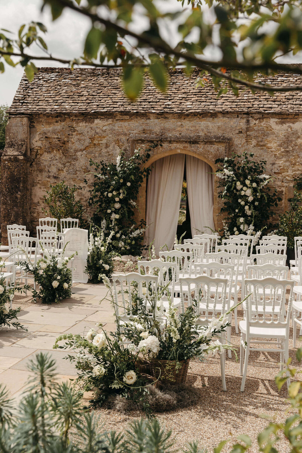 Outdoor wedding ceremony at Caswell House with white and green florals against Cotswold stone backdrop