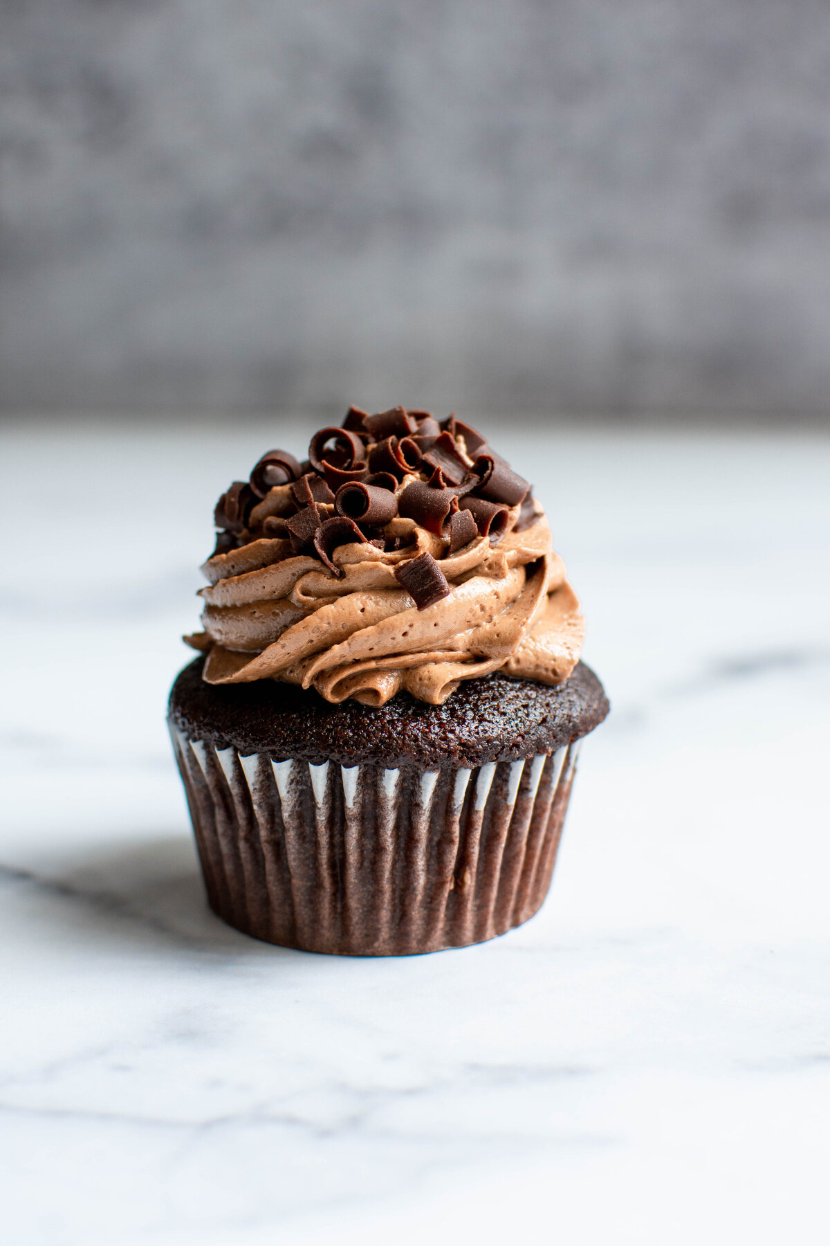 Chocolate cupcake with chocolate frosting and curled chocolate shavings on a light marble surface