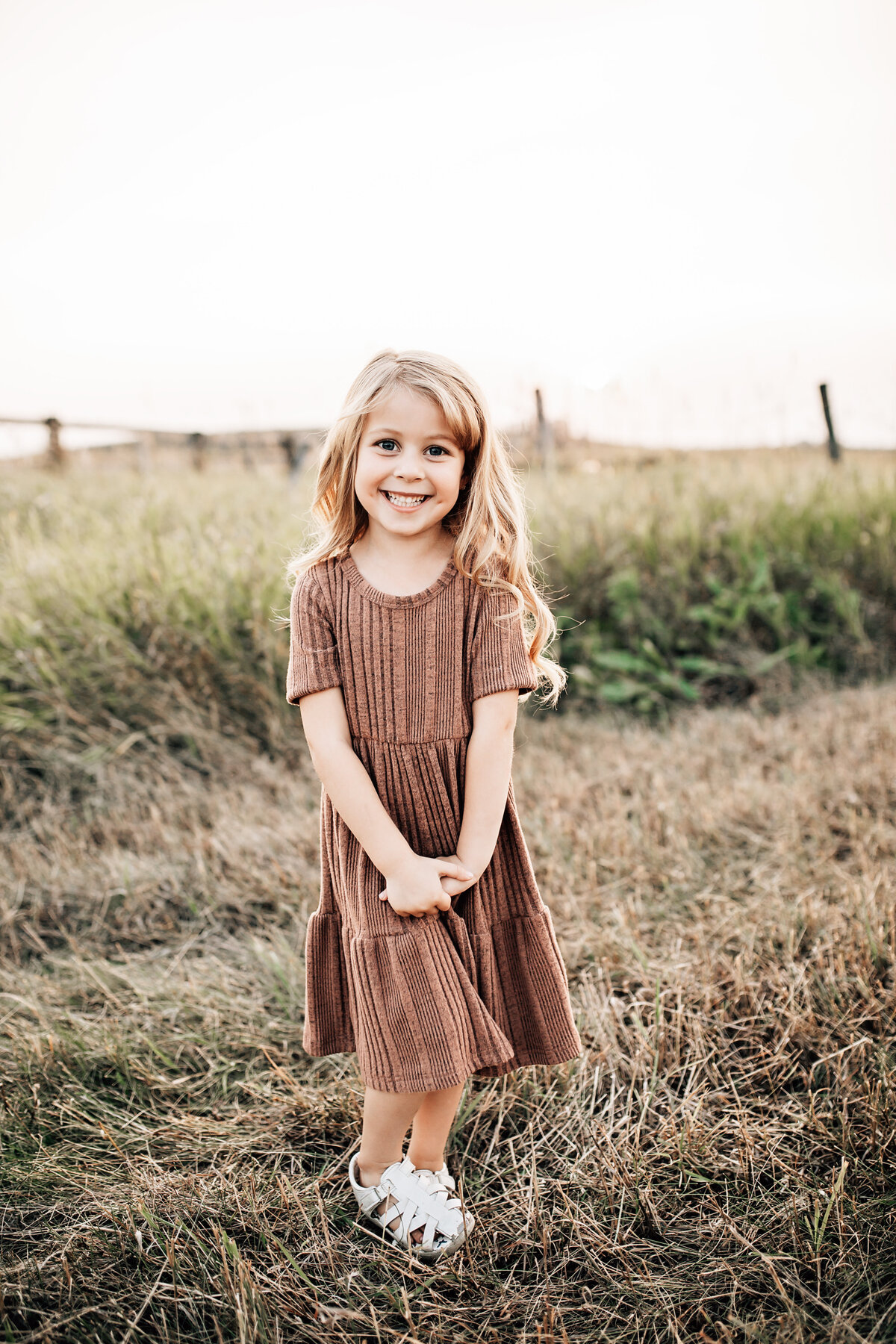 little girl at sunset smiling in brown dress