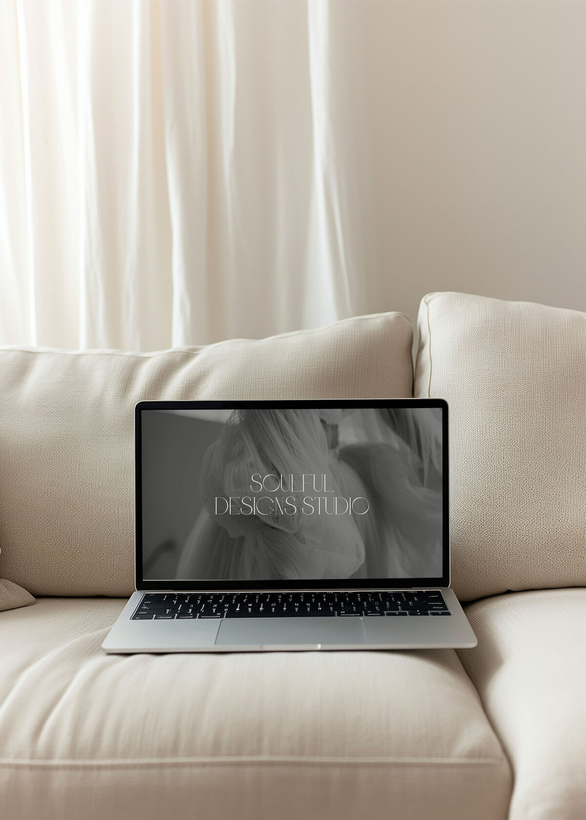 An opened laptop mockup on a beige couch with a soulful designs studio brand wallpaper