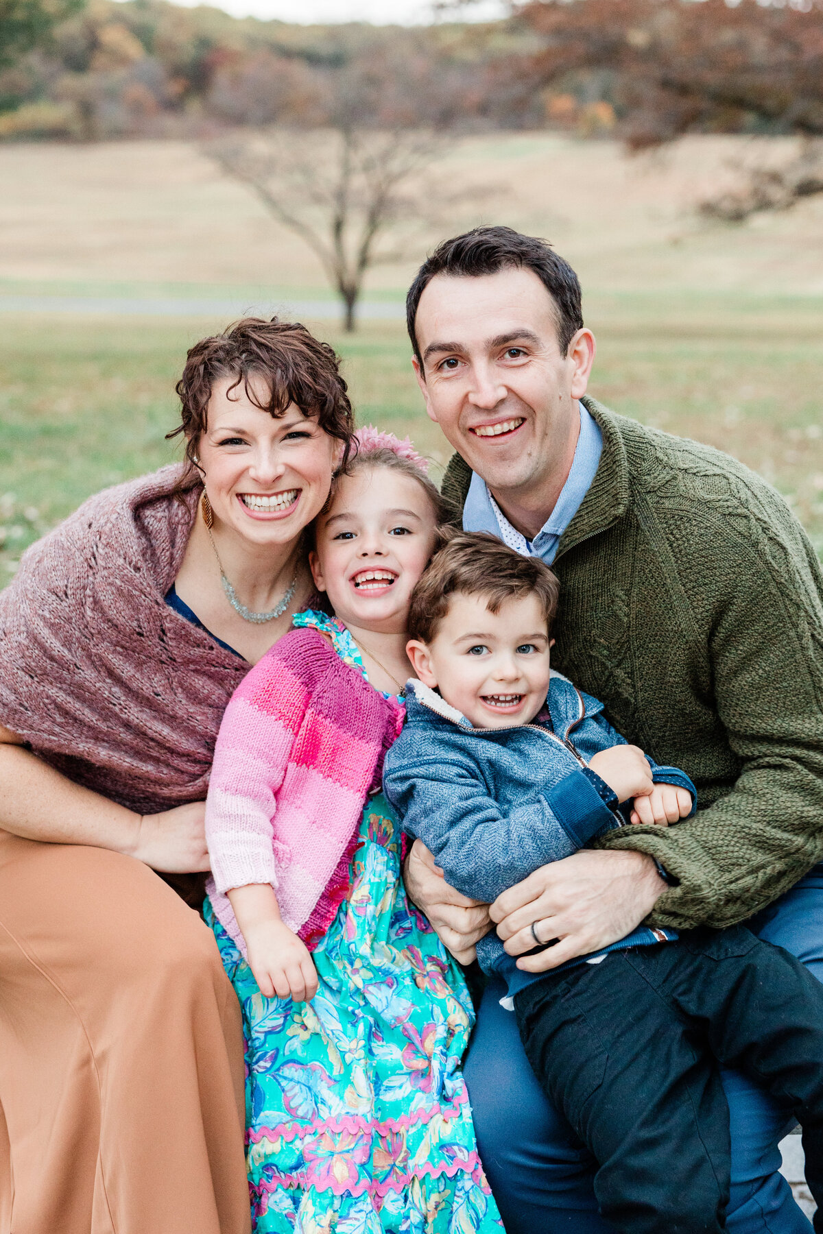 Family of four snuggling on park bench wearing bright colored outfits