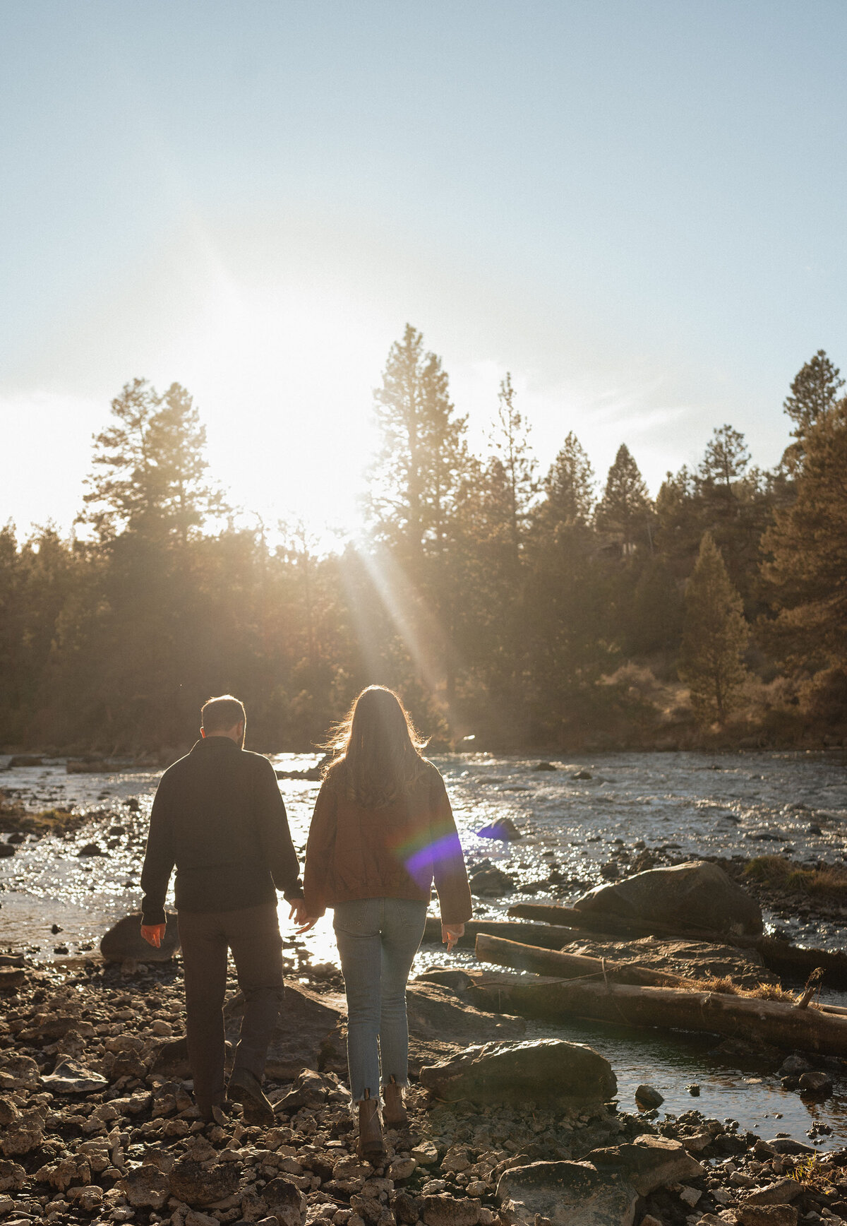couple holds hands while walking along the river during sunset in Bend, Oregon