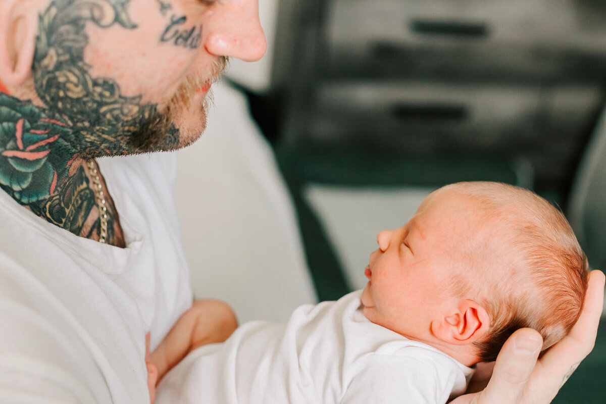 A new father in a white shirt looks down at his newborn baby