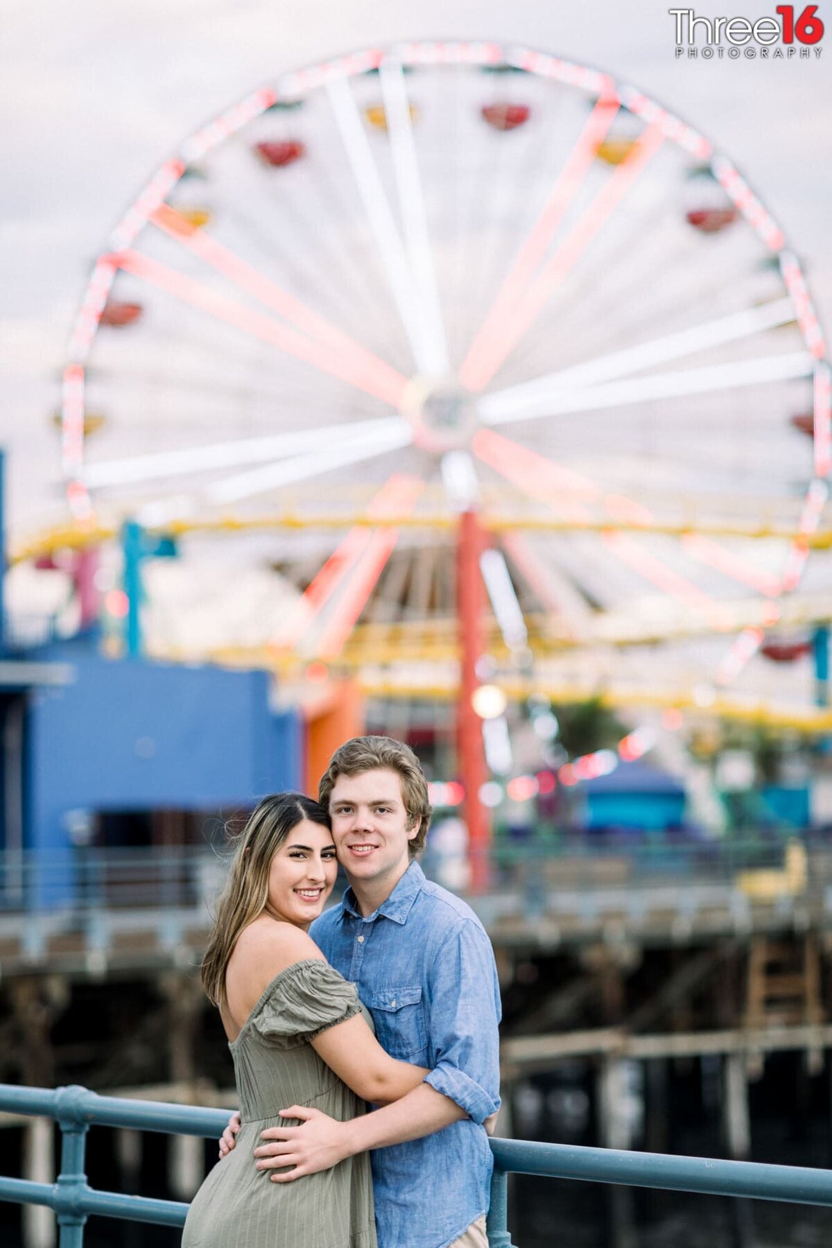 Engaged couple embrace each other with the Santa Monica Pier in the background