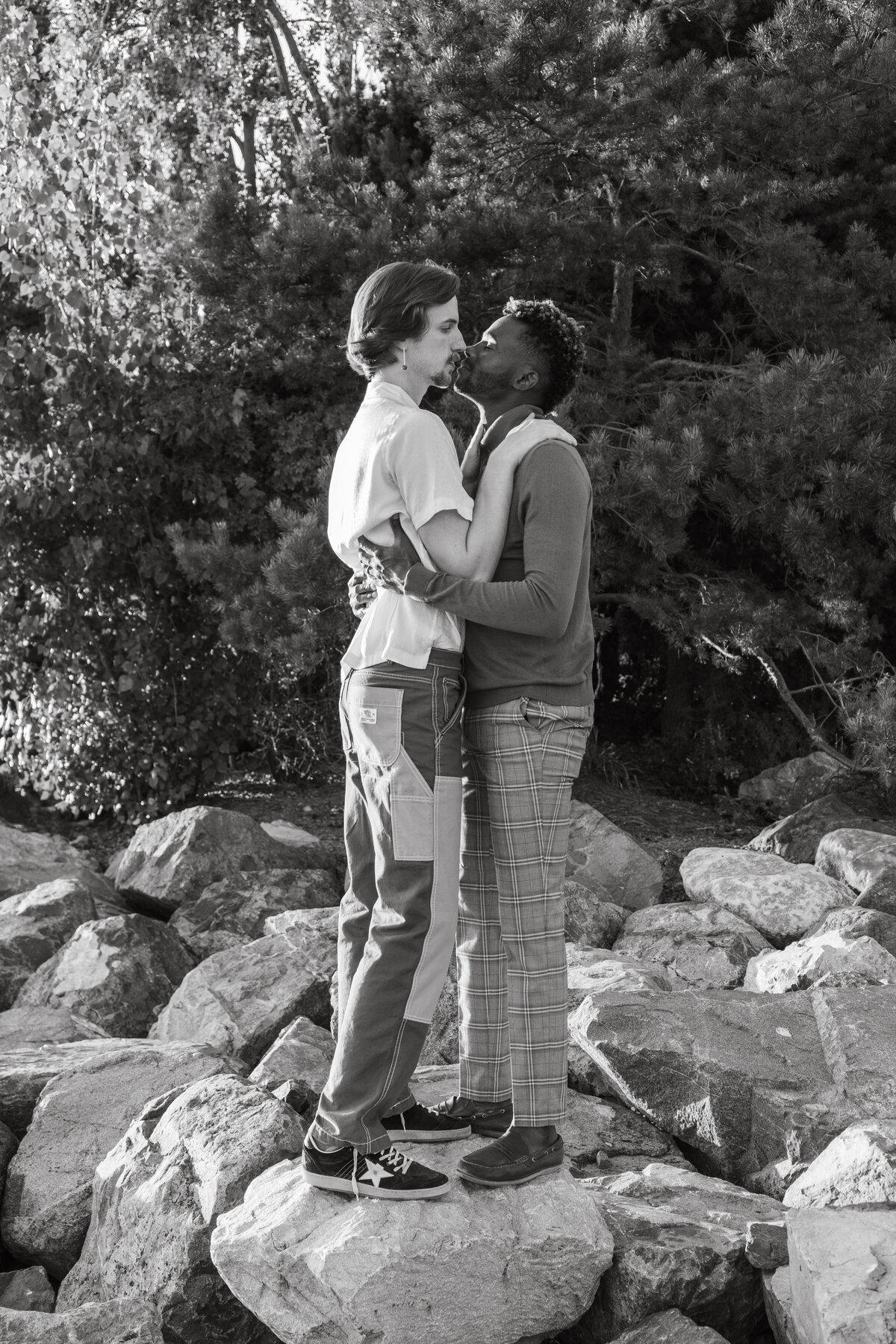 Black and white portrait of an engaged queer couple kissing at Pocket Beach in Seattle during sunset.