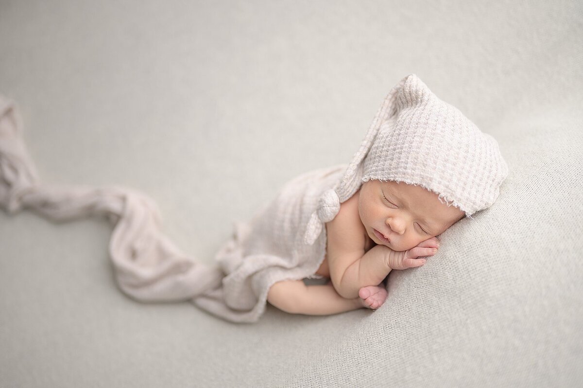 Baby sleeping with hand under face in neutral wrap and hat at Always Images Mishawaka newborn photographer