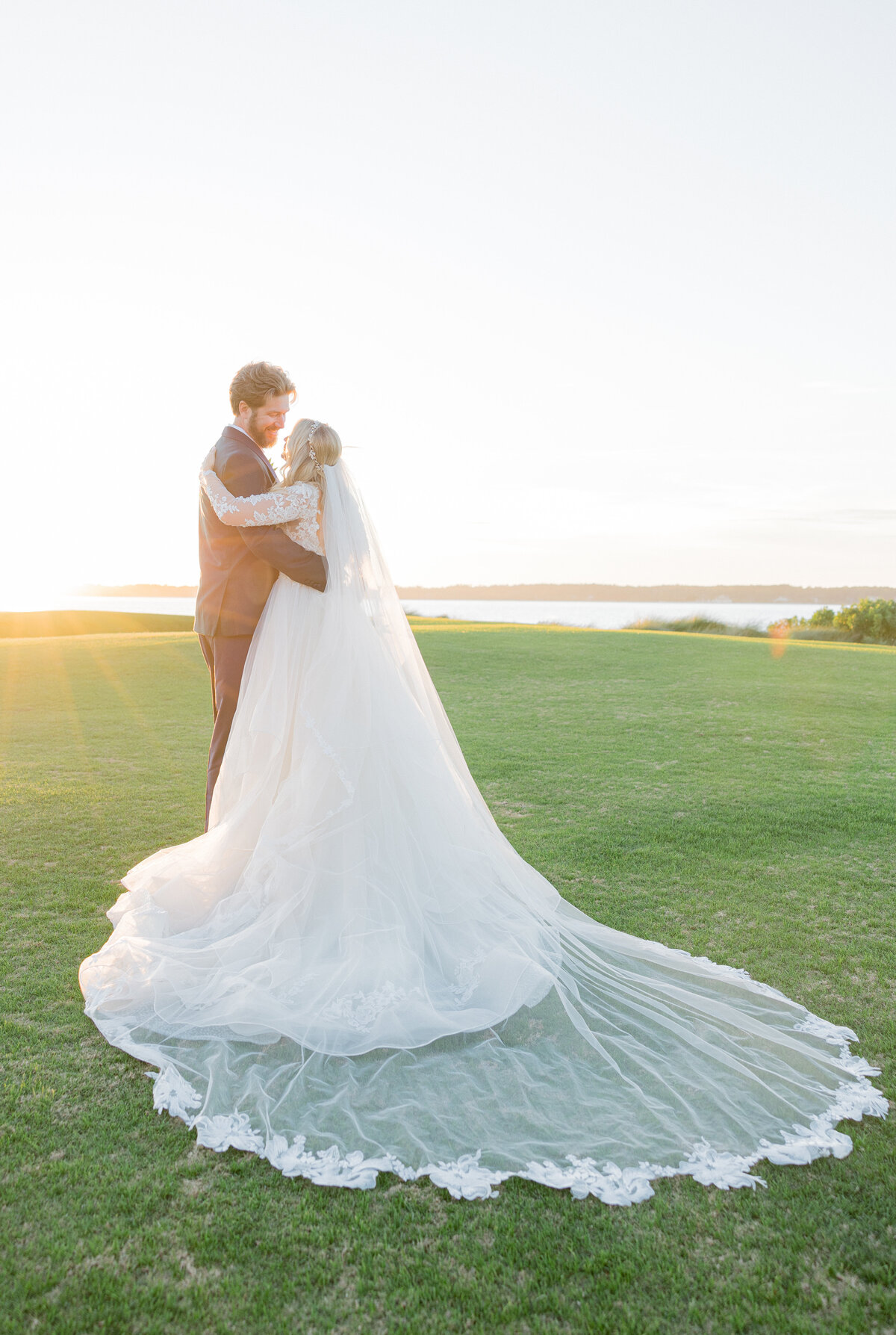 Bride and groom embrace at sunset on the waterfront lawn of Sea Pines Resort, Hilton Head Island—captured by luxury wedding photographer Amia Marcell.
