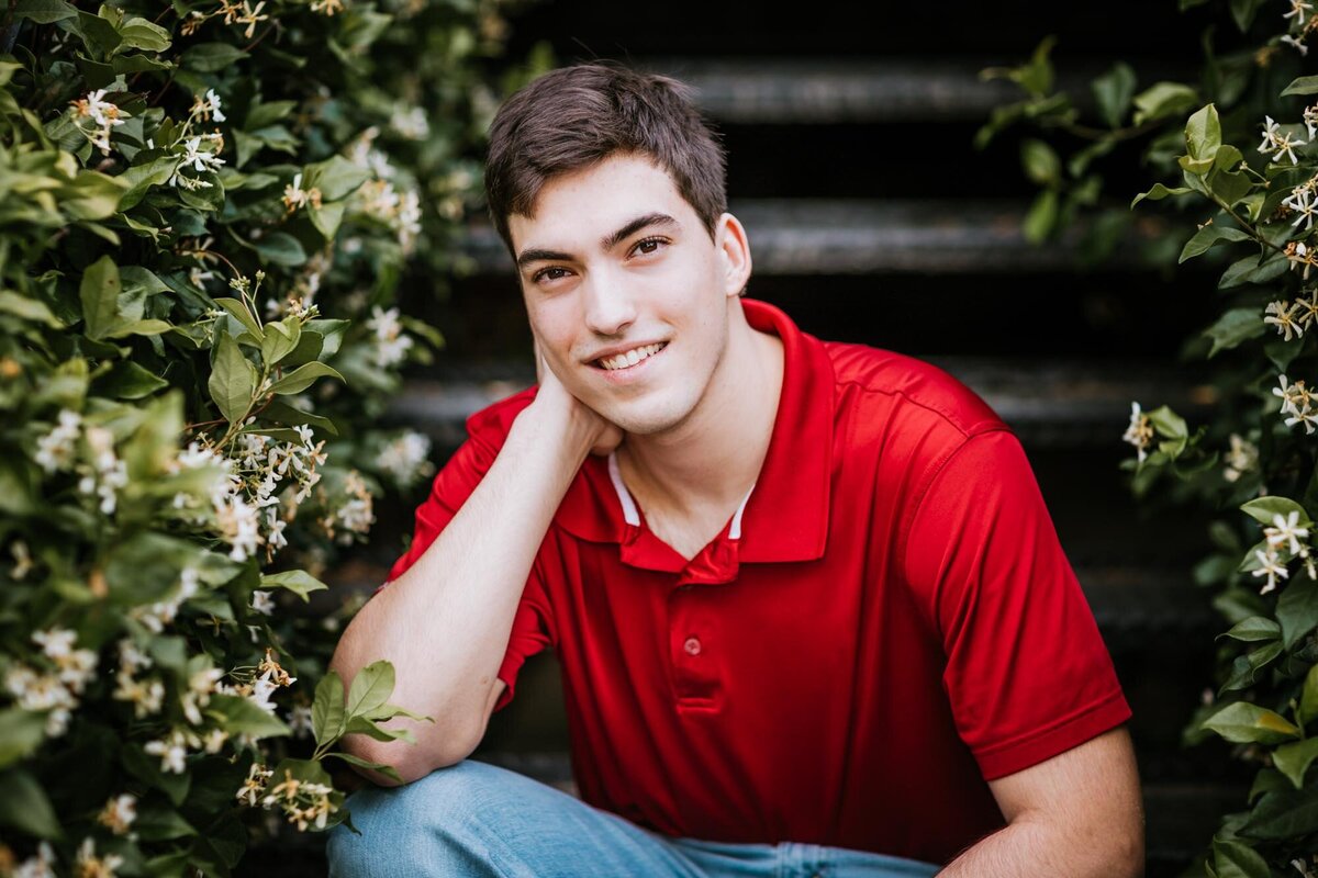 A guy sitting on steps wearing a red shirt and smiling big for the portrait.