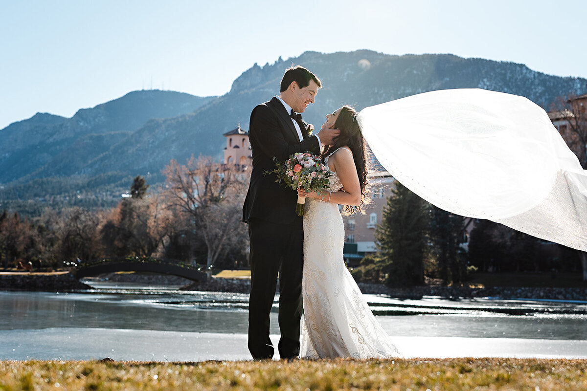 Bride's veil blows in the wind with her groom on their wedding day.