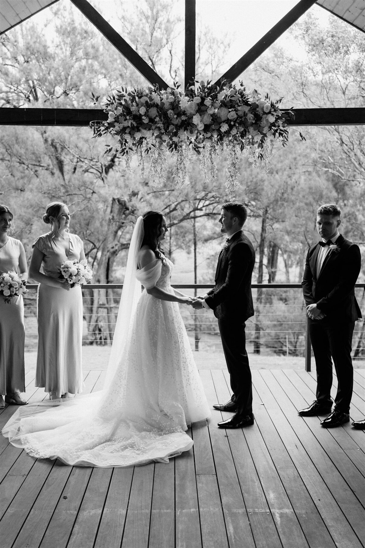 The bride, radiant in her flowing white gown, exchanges heartfelt vows with her groom under a canopy of blooming roses.
