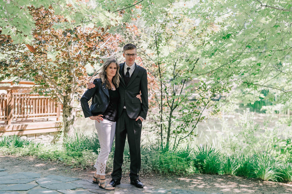 Standing with his mom in front of trees with pink flowers. 