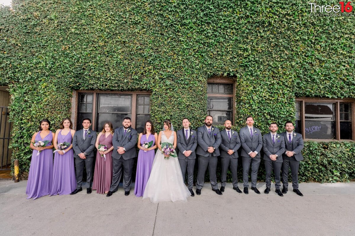 Bride and Groom pose with bridal party outside the venue in front of ivy filled side of a building
