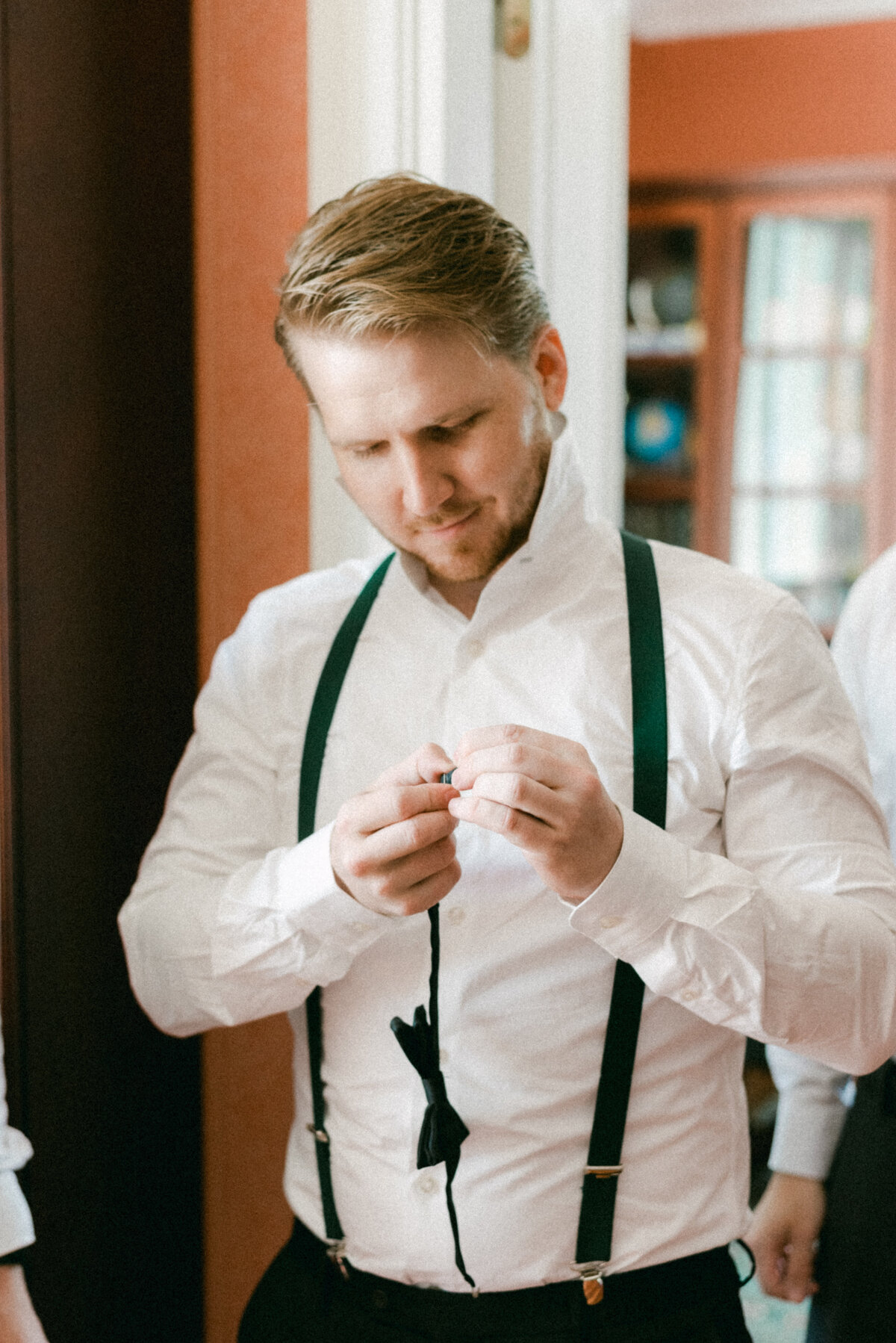 The groom is adjusting his bowtie in an image captured by wedding photographer Hannika Gabrielsson.
