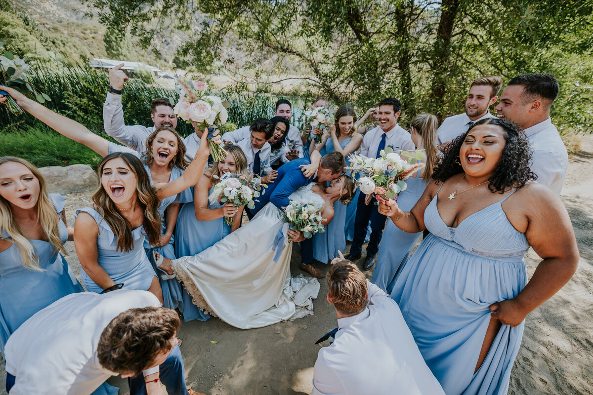 Groom dips bride for a kiss while bridal party surrounds them and celebrates.