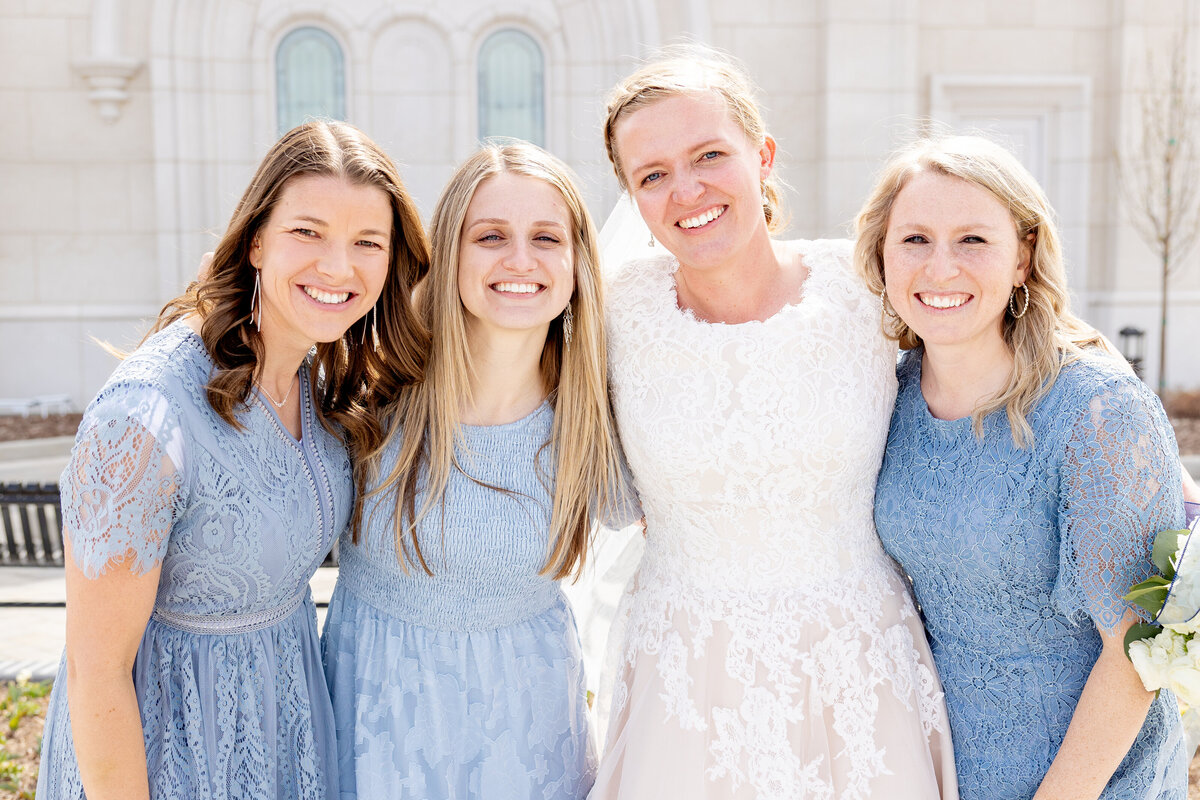 The bride and her bridesmaids pose closely together, smiling happily on the temple grounds.