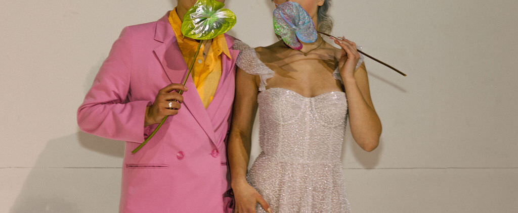 A newlywed couple holding flowers over their mouths.