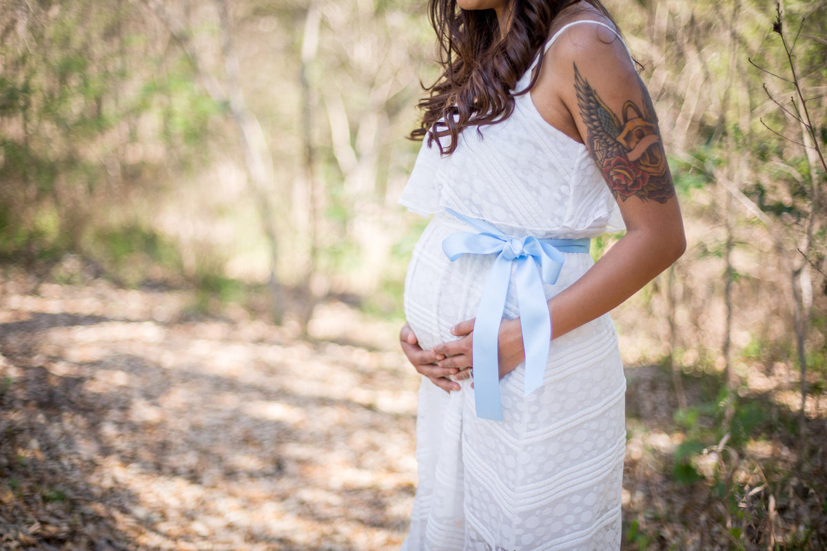 Pregnant mother with tattoos holding belly standing in Walker Ranch Historic Landmark Park in San Antonio maternity photo.