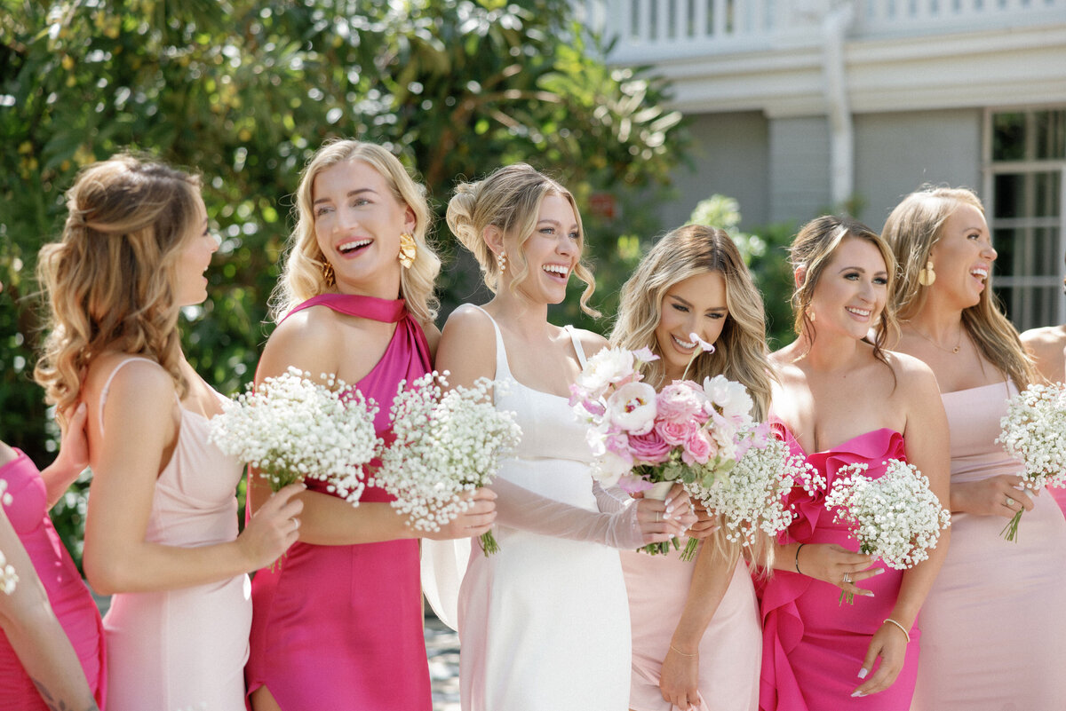 Bride and bridesmaids dressed in pink laughing together at wedding.