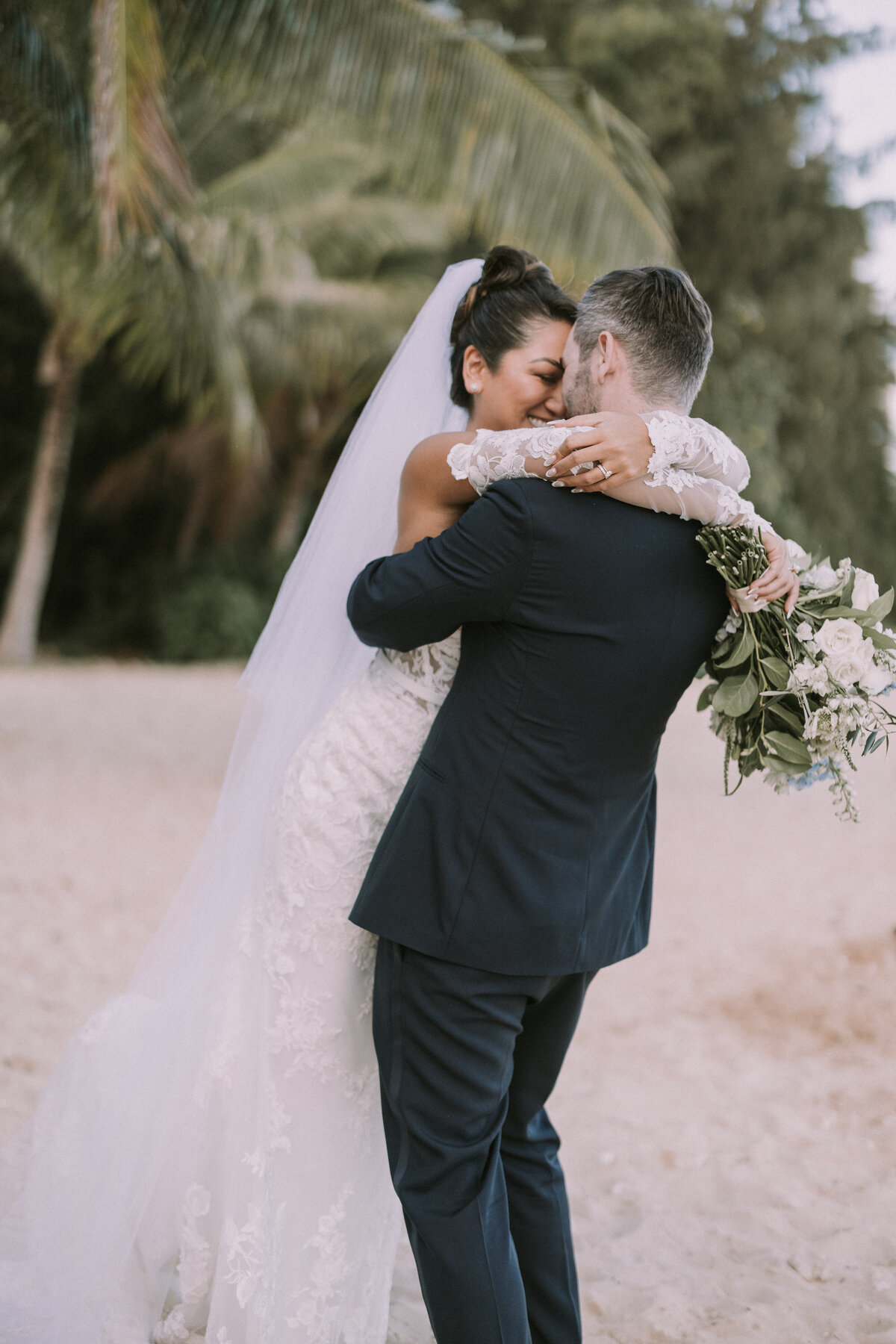 Wedding couple hugging holding wedding bouquet on the beach with tropical feels