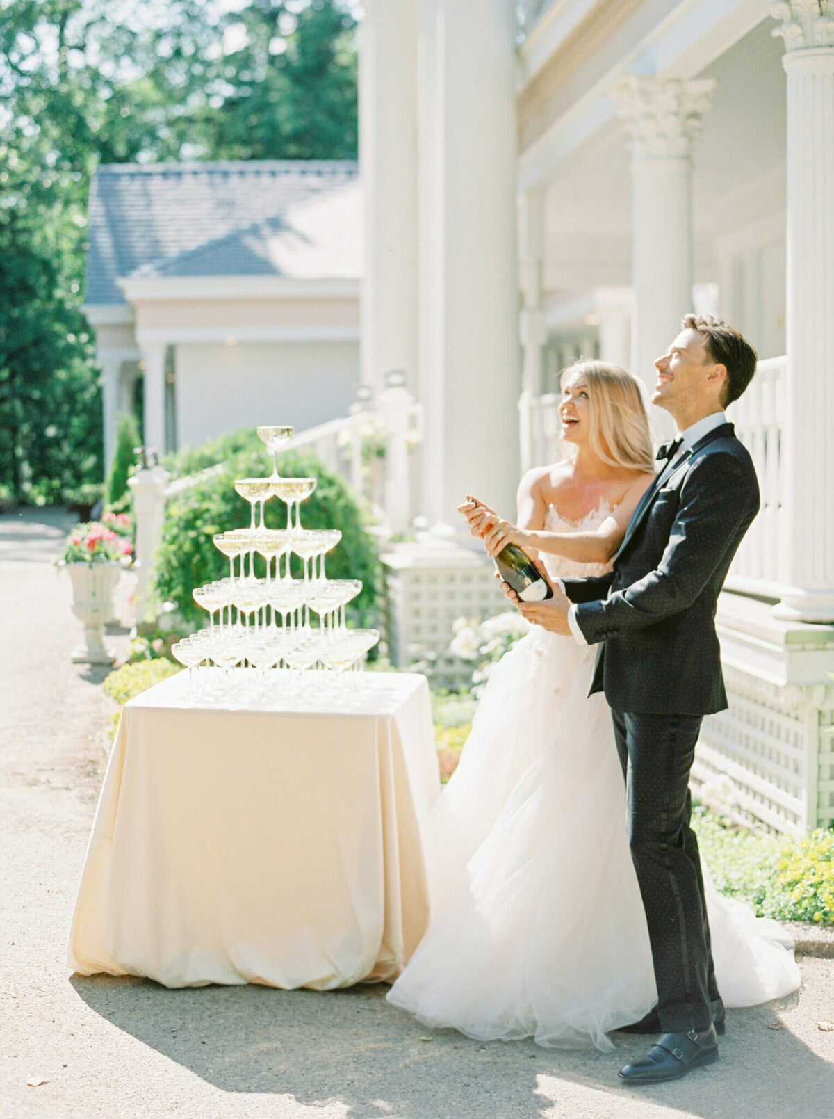 Bride and groom popping champagne in front of The Norland Historic Estate, a classic vintage wedding venue in Lethbridge, AB, featured on the Brontë Bride Vendor Guide.