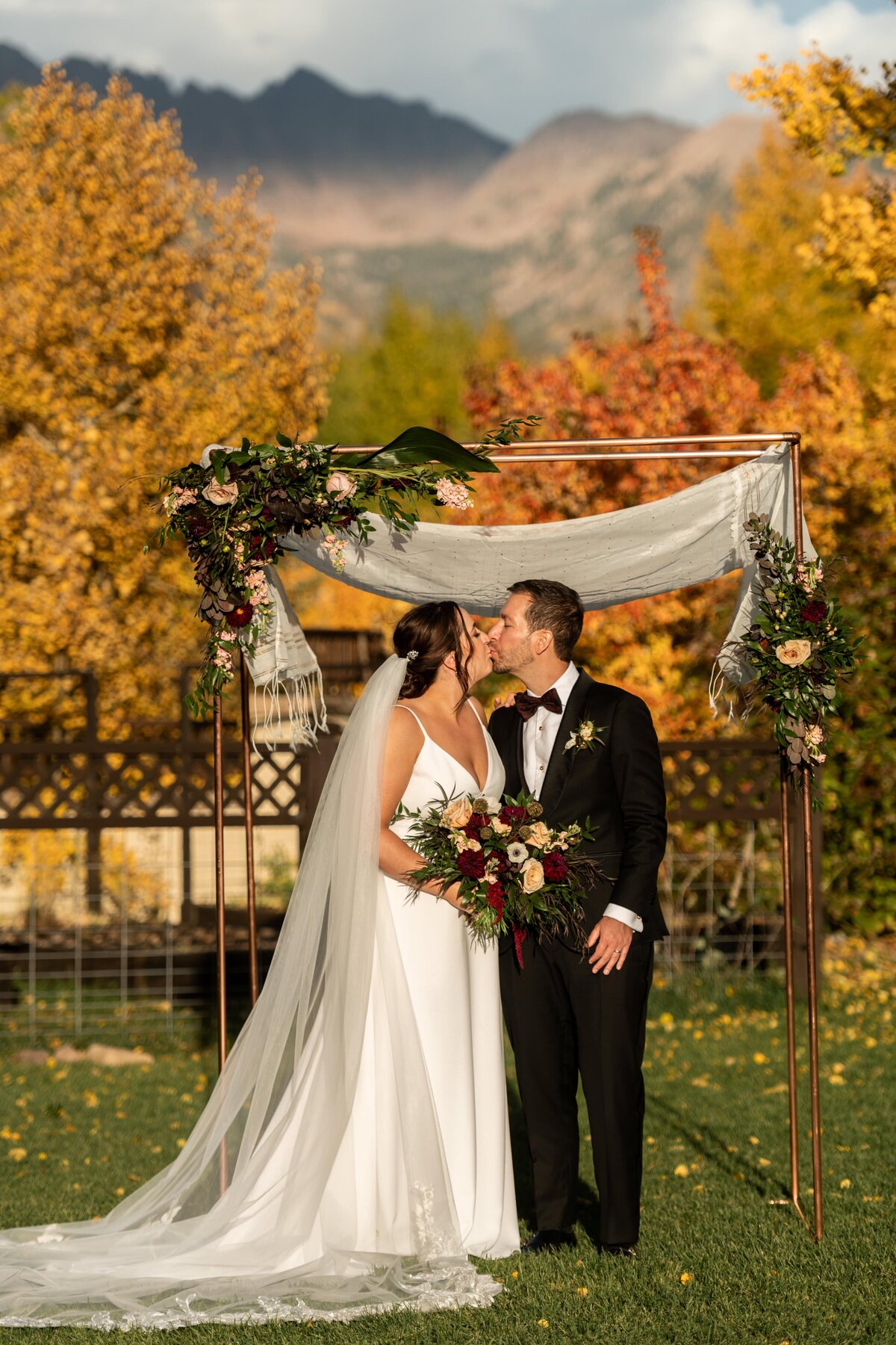 Bride and groom share their first kiss during their wedding ceremony under their chuppah in Vail, Colorado.