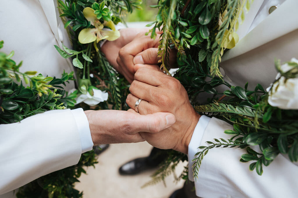 A close up of a wedding ring on a hand with florals around it.