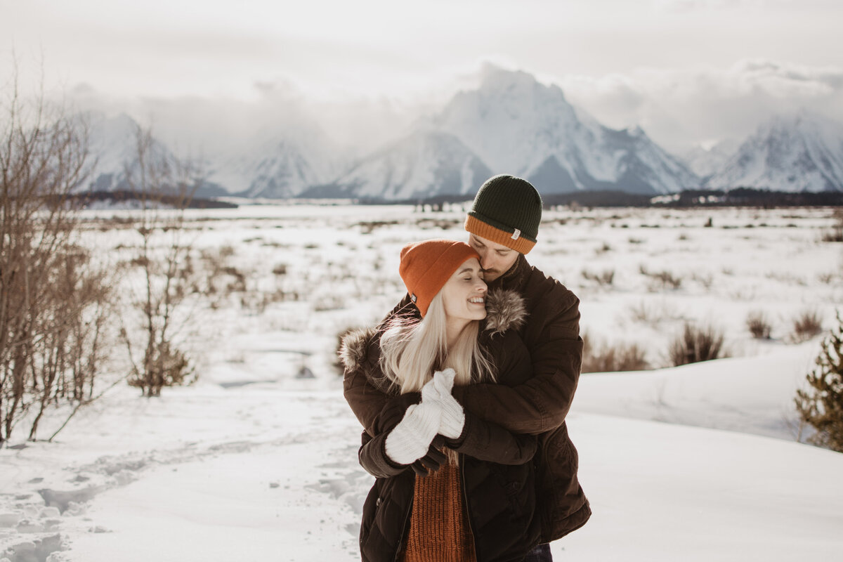jackson hole photographers captures man holding woman from behind with his arms around her shoulders in the Grand Tetons for their winter engagement session