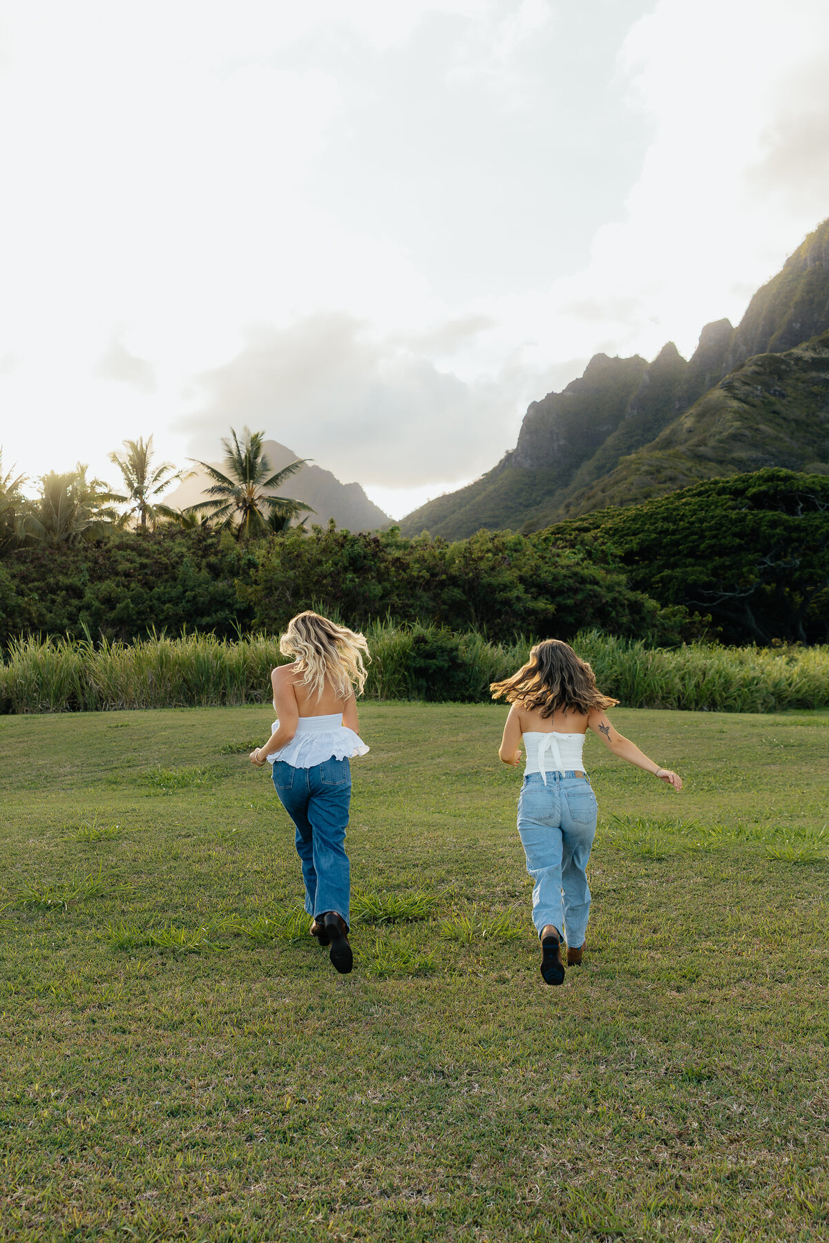 Two best friends running together with mountain backdrop at photoshoot in Oahu