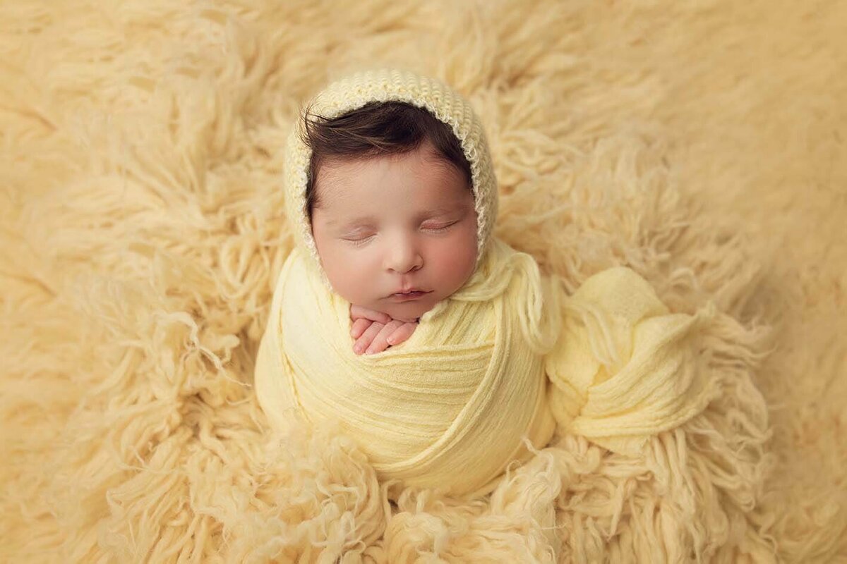 baby girl wearing a yellow wrap and yellow bonnet asleep sitting up