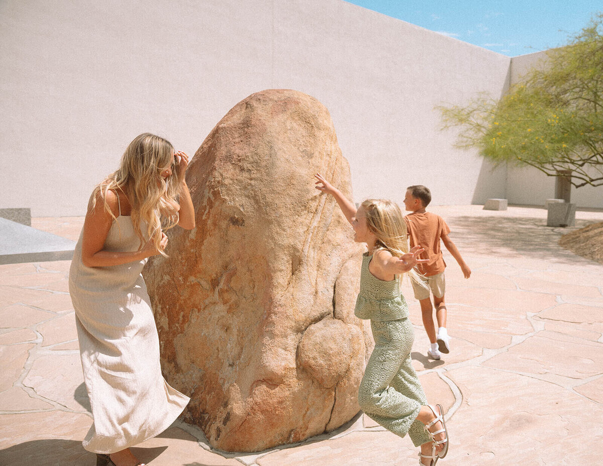 Mom and two kids playing around a large stone sculpture at Noguchi Garden in Costa Mesa during a candid family photo session.