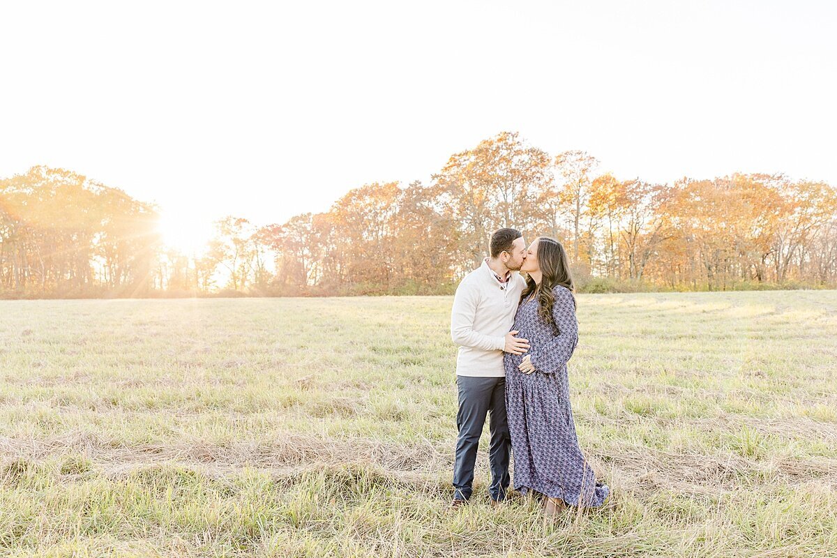 couples kisses in field  during winter maternity photo session with Sara Sniderman Photography at Heard Farm in Wayland Massachusetts