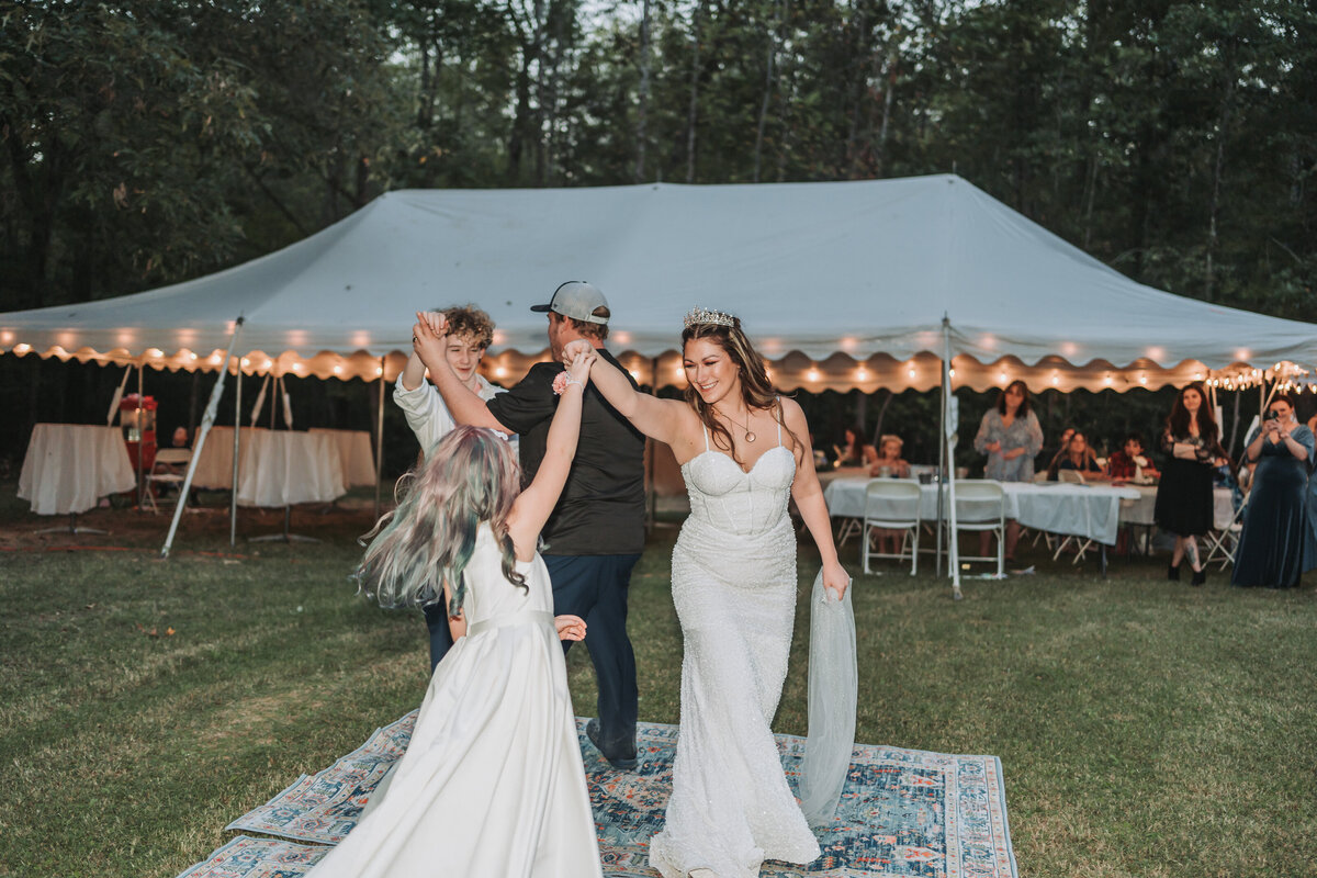 A happy bride in her wedding gown dances with guests on a patterned rug under a large white reception tent, surrounded by celebrating attendees at a Virginia wedding, captured by Quinn Photography LLC.