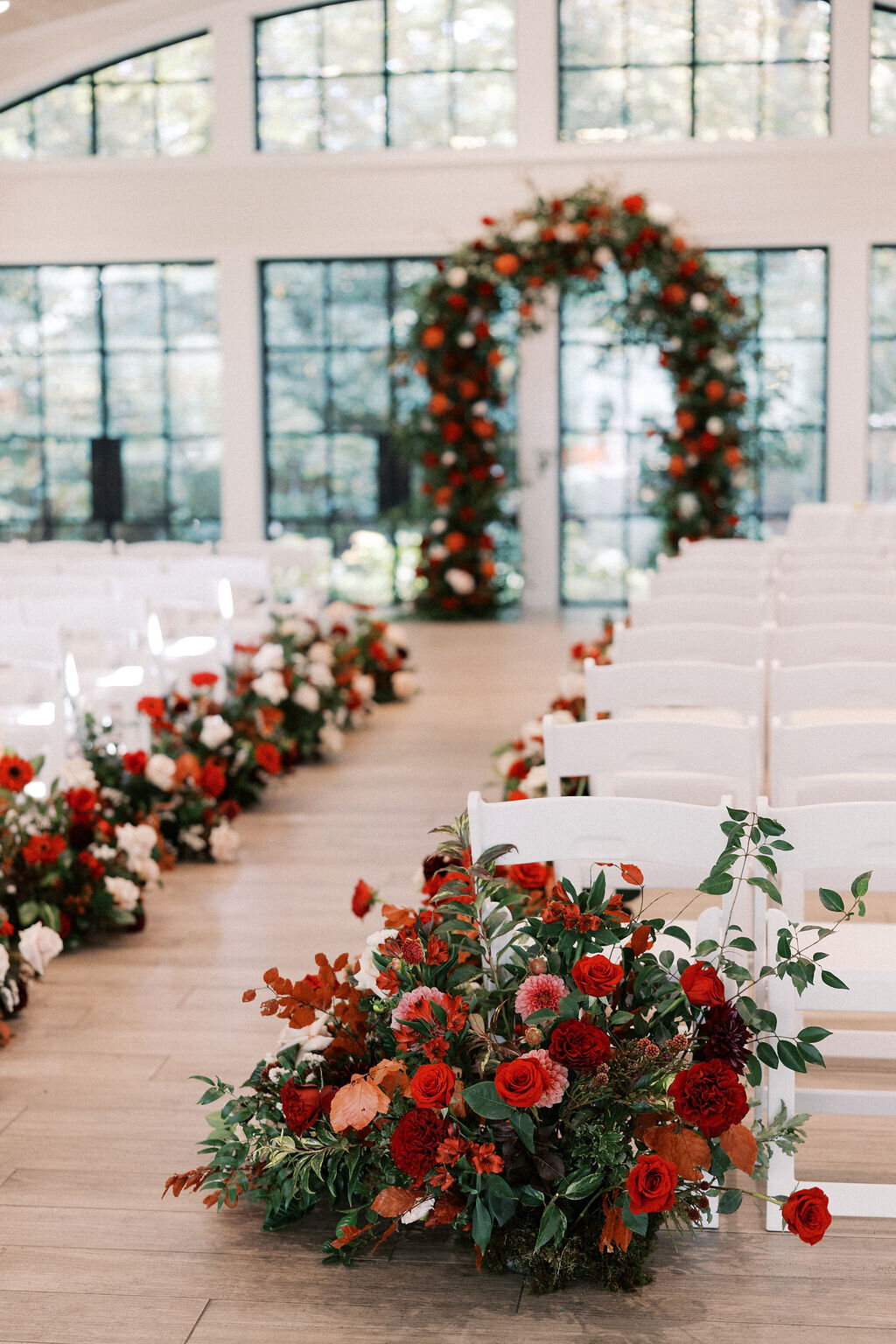 Indoor wedding ceremony with tall floral arch and aisle lined with red and blush florals at Old Edwards Inn.