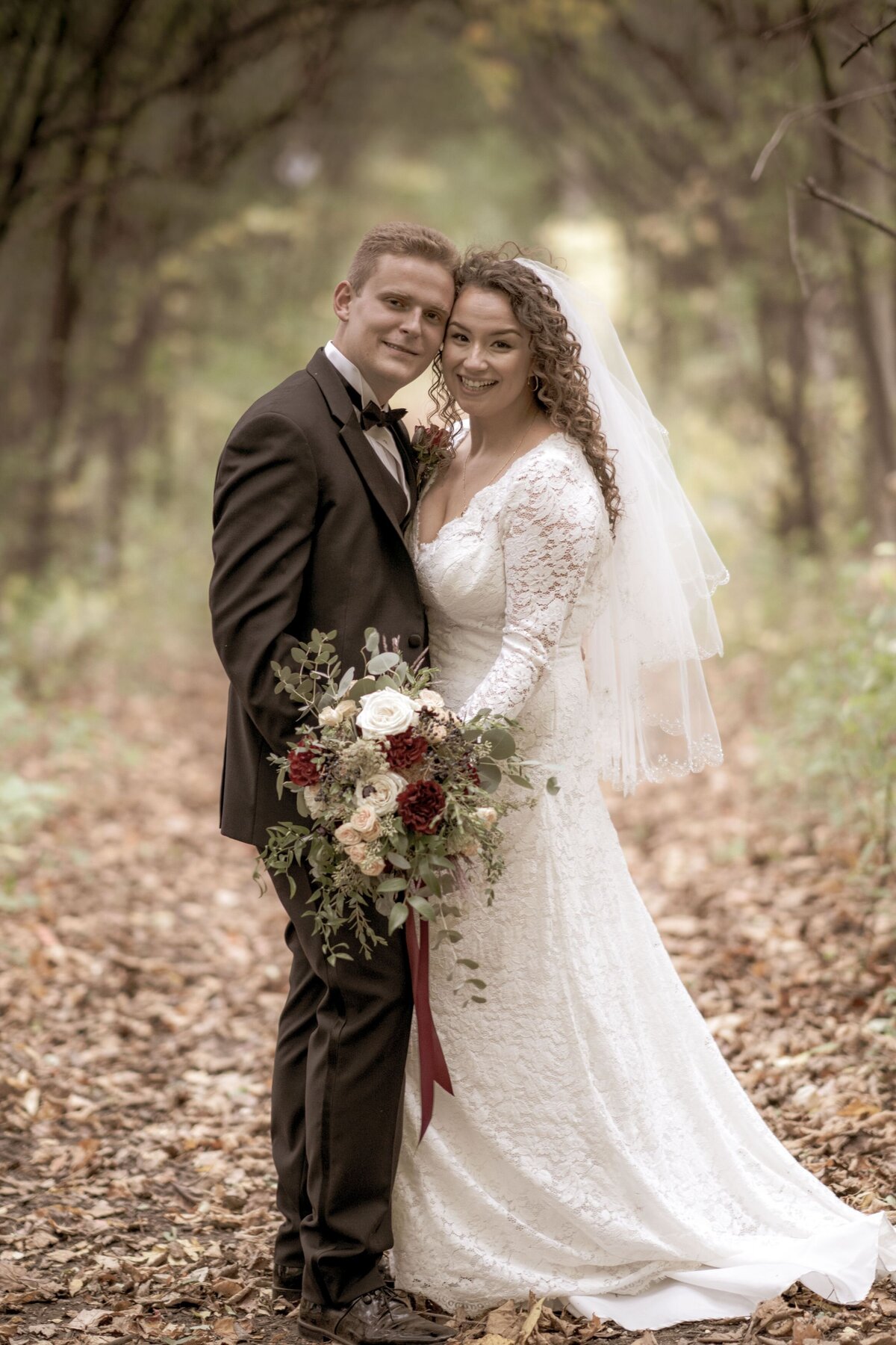 The bride and groom pose together amidst a picturesque fall forest. The vibrant autumn foliage creates a warm and romantic backdrop, highlighting the couple's love and connection. The rich colors of the fall leaves complement their wedding attire, adding a seasonal touch to their beautiful and serene outdoor portrait.