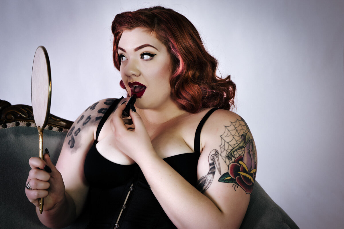 Red haired girl with tattoos applying her lipstick with a vintage mirror in the twin cities.
