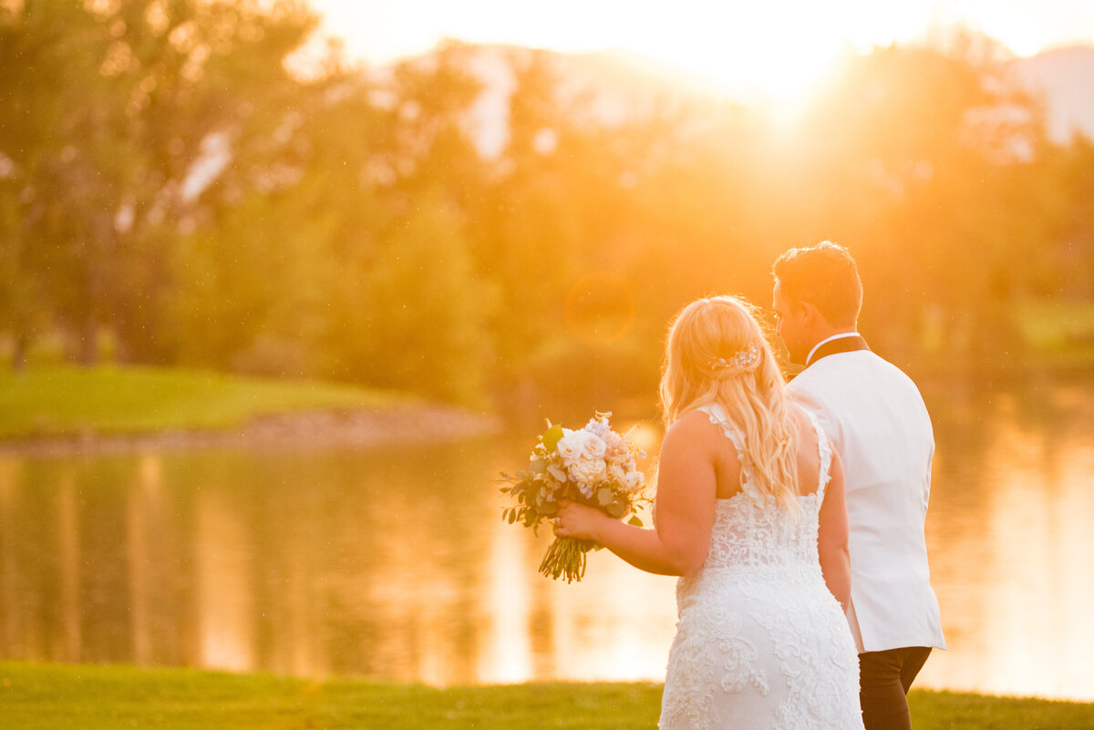 A bride and groom walk away from the camera in front of a lake at golden hour at The Barn at Raccoon Creek.
